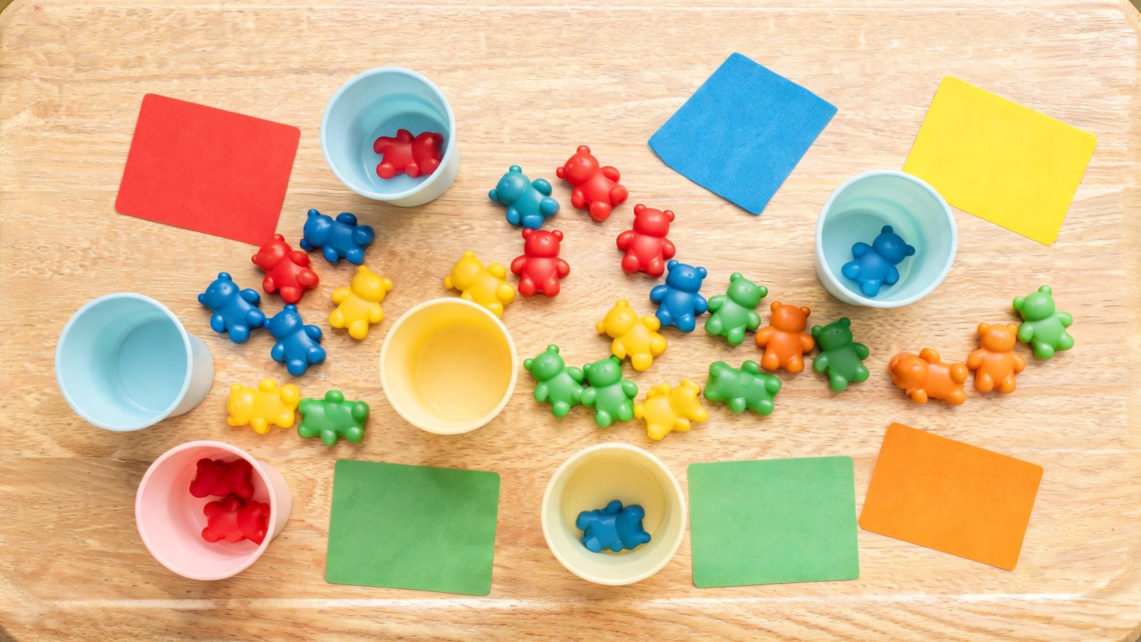 Illustrative image: counting bears, small cups and plain colored cards on a play table.