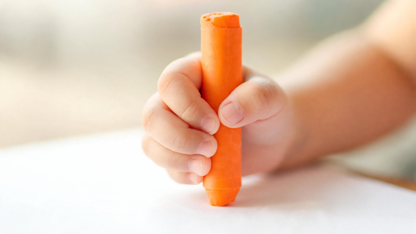 Illustrative image: a young child's hand holding a short crayon above paper.